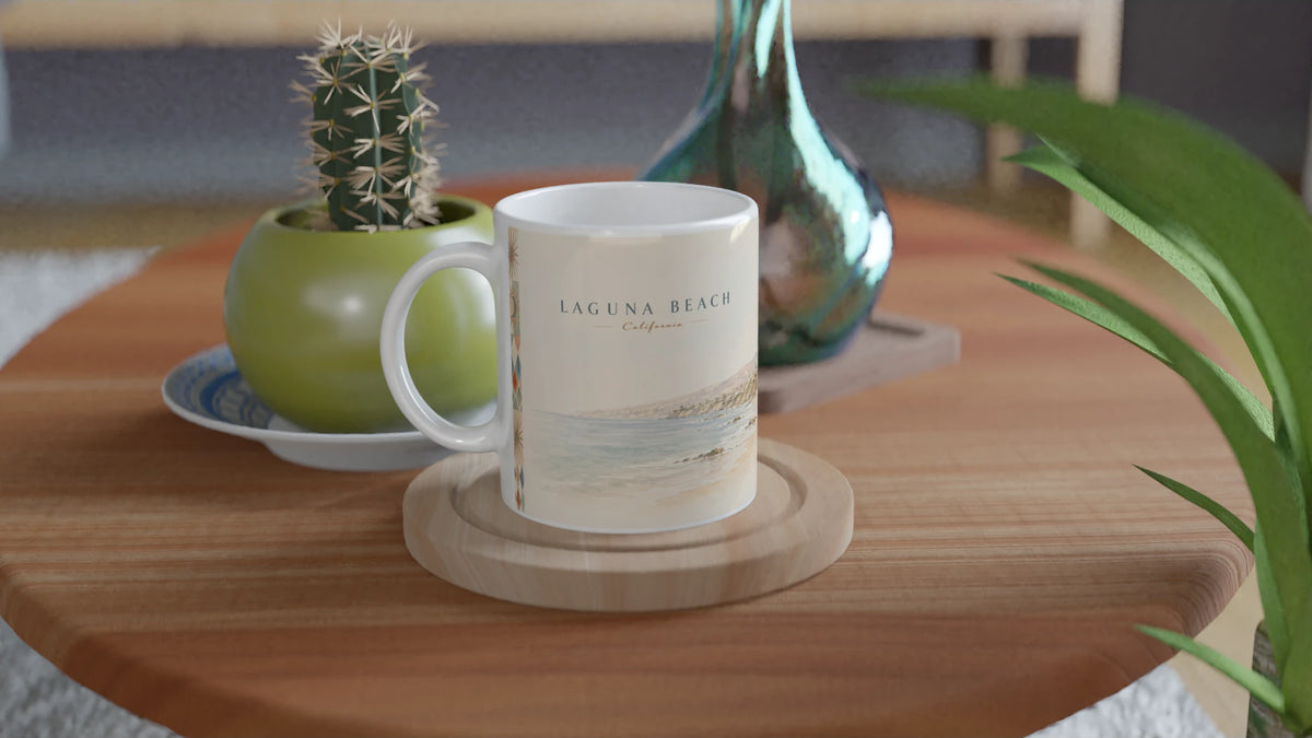 Laguna Beach California Keramiktasse mit nostalgischem Küsten-Aquarell auf einem Holztisch in einem Wohnambiente mit kleinem Kaktus, Glasvase und grüner Pflanze
