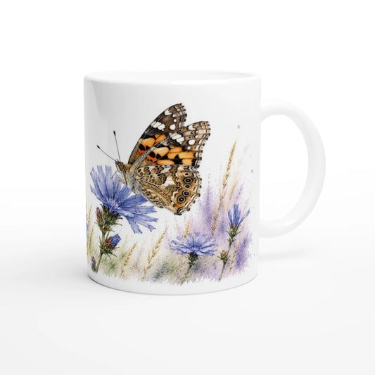Keramiktasse mit Distelfalter auf blauen Wildblumen in einer sanften Aquarellwiese