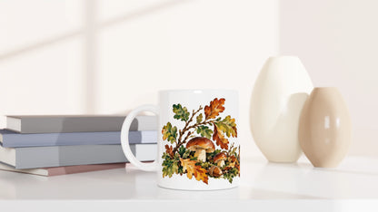 Weiße Tasse mit herbstlicher Waldszene aus Igel, Laub, Pilzen und Eicheln in Ocker-, Braun-, Grün- und Rosttönen.