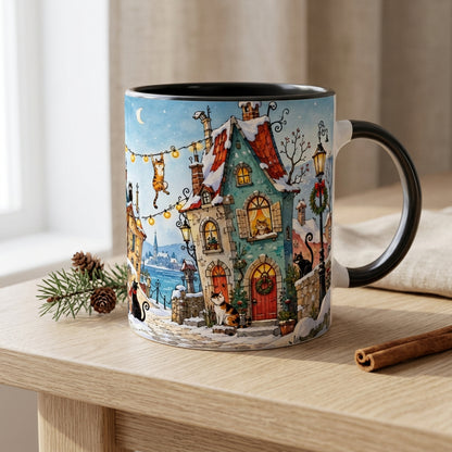 Weihnachtliche Keramiktasse mit einem verschneiten Winterdorf, neugierigen Katzen und einem festlich geschmückten Weihnachtsbaum. Das Katzenmotiv auf der weißen Tasse bringt gemütliche Adventsstimmung zum Ausdruck.
