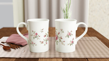 Rosen Porzellantasse mit botanischer Illustration in sanften Rosa-, Creme- und Grüntönen. Zarte Blüten und Rosenknospen bilden eine klassische, nostalgische Blumenkomposition.