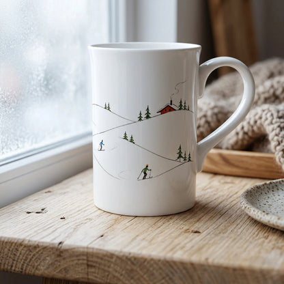 Schlanke weiße Porzellantasse mit minimalistischer Winterlandschaft und Skifahrern als Wintermotiv; Produktansicht der 295-ml-Tasse mit Henkel.