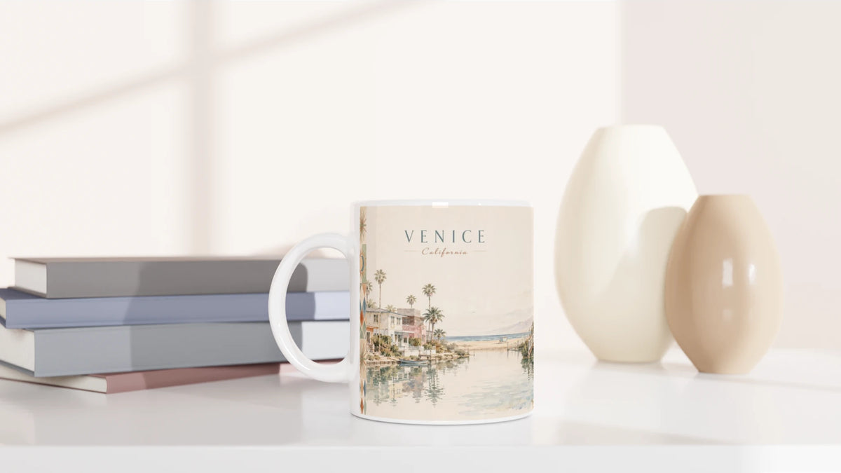 Venice California Keramiktasse mit hellem Retro-Aquarell von Kanälen und Palmen in einem modernen Wohnambiente neben Büchern und dekorativen Vasen
