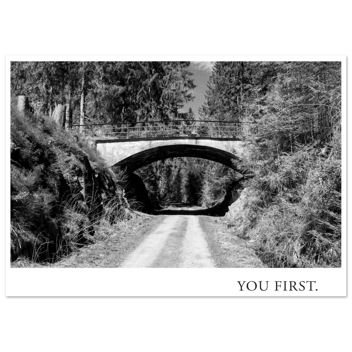 Schwarzweiß Fotografie Kunstdruck YOU FIRST mit einer alten Bogenbrücke über einem einsamen Waldweg, fotografiert 2022 und gestaltet als Fine Art Print von Mano et Arte