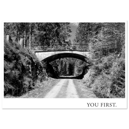 Schwarzweiß Fotografie Kunstdruck YOU FIRST mit einer alten Bogenbrücke über einem einsamen Waldweg, fotografiert 2022 und gestaltet als Fine Art Print von Mano et Arte