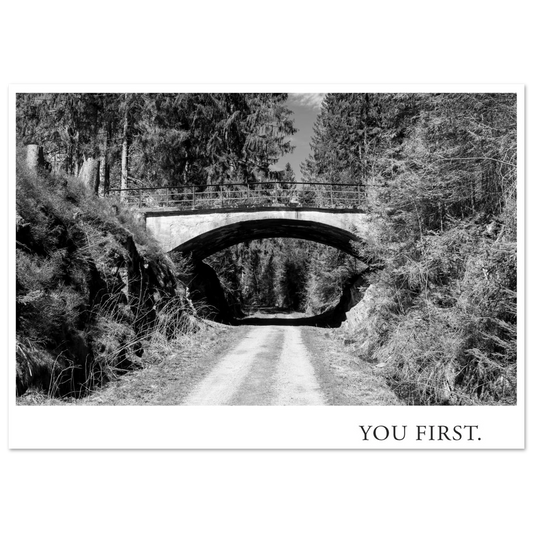 Schwarzweiß Fotografie Kunstdruck YOU FIRST mit einer alten Bogenbrücke über einem einsamen Waldweg, fotografiert 2022 und gestaltet als Fine Art Print von Mano et Arte