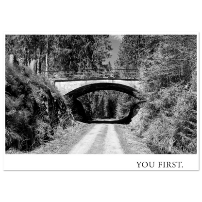 Atmosphärische Schwarzweiß Fotografie eines Waldweges unter einer alten Bogenbrücke mit dem typografischen Statement YOU FIRST als moderne Fotokunst
