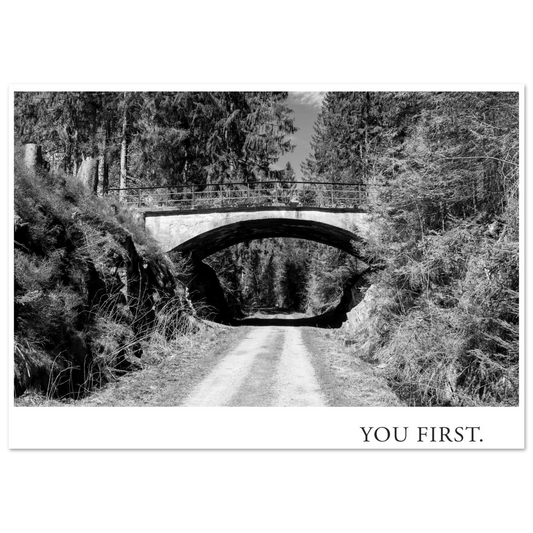 Atmosphärische Schwarzweiß Fotografie eines Waldweges unter einer alten Bogenbrücke mit dem typografischen Statement YOU FIRST als moderne Fotokunst
