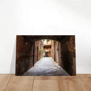 Aluminiumbild mit historischer, schmaler Gasse in Siena unter einem dunklen Torbogen, warmen Backsteinwänden und hellem Ausgang im Hintergrund.