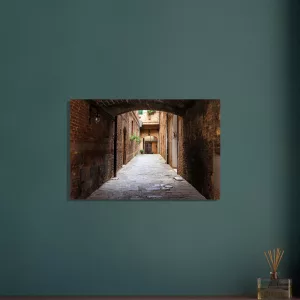 Aluminiumbild mit historischer, schmaler Gasse in Siena unter einem dunklen Torbogen, warmen Backsteinwänden und hellem Ausgang im Hintergrund.